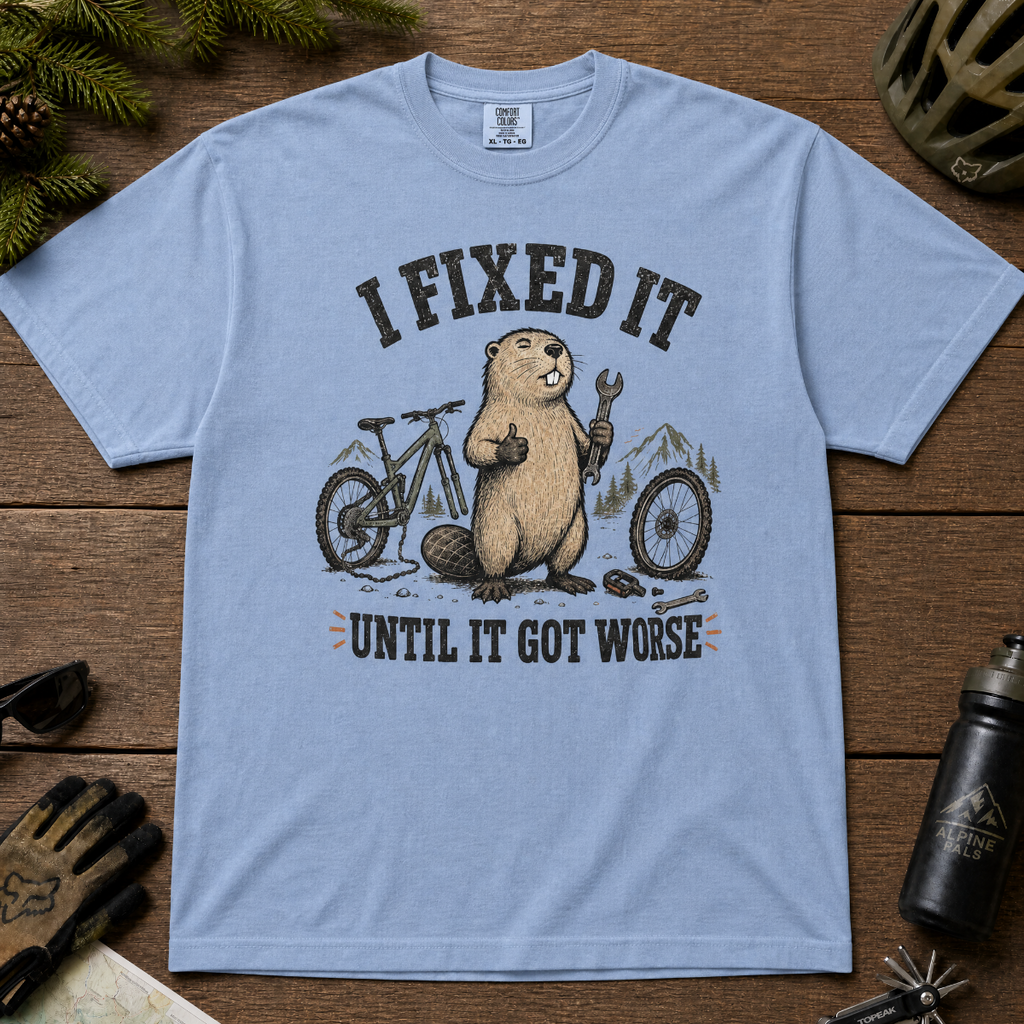 Washed denim blue t-shirt with beaver graphic and text on a wooden surface with cycling accessories.