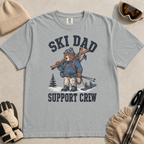 Flat lay of a granite gray t-shirt featuring a tired bear carrying skis and ski gear, with “Ski Dad Support Crew” text.