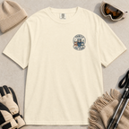 Flat lay of an ivory white t-shirt featuring a small chest “Family Ski Team” badge graphic with three winter animal characters, styled with ski accessories.