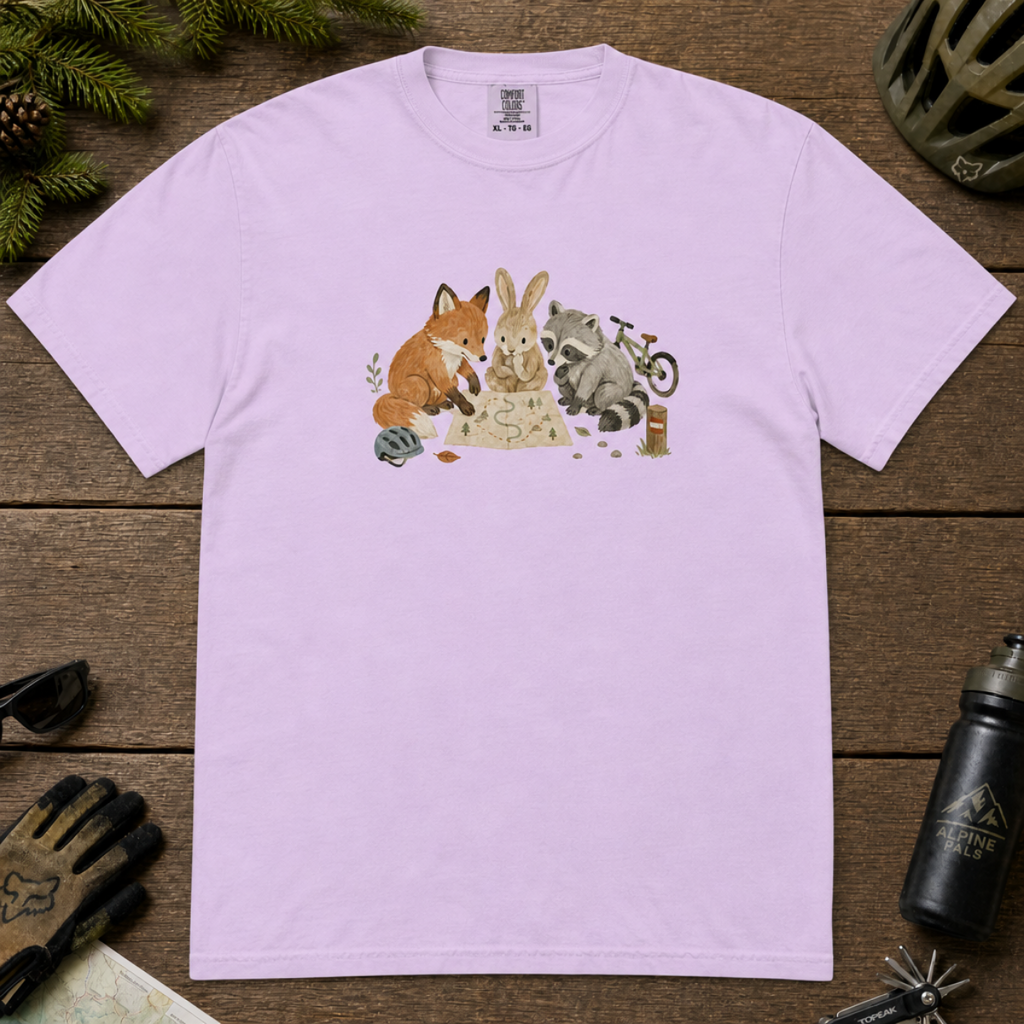 Flat lay of a orchid coloured t-shirt featuring a cute woodland animal trail-planning graphic with a fox, rabbit, raccoon, map, helmet, bike, and trail marker.