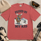 Flat lay of a crimson red t-shirt featuring a funny “Passed By My Kid” ski design with a humbled moose watching a small rabbit snowboarder pass by.