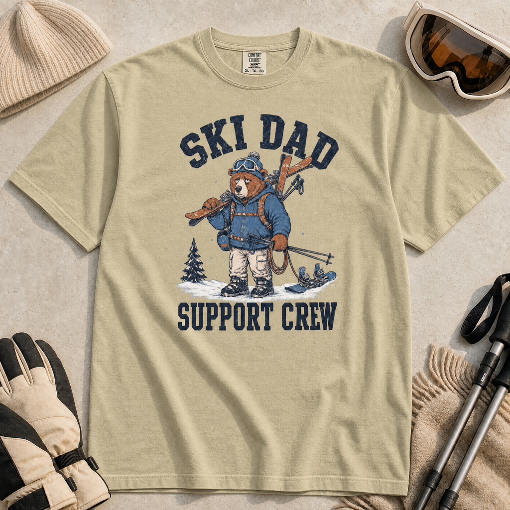 Flat lay of a khaki t-shirt featuring a tired bear carrying skis and ski gear, with “Ski Dad Support Crew” text.