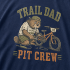 Close-up of a navy t-shirt with a funny “Trail Dad Pit Crew” design showing an exhausted beaver repairing a small mountain bike.