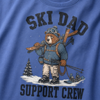 Close-up of a mystic blue t-shirt with a vintage ski dad design showing an exhausted bear loaded with skis, poles, and snow gear.
