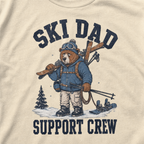 Close-up of an ivory white t-shirt with a vintage ski dad design showing an exhausted bear loaded with skis, poles, and snow gear.