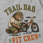 Close-up of a granite gray t-shirt with a funny “Trail Dad Pit Crew” design showing an exhausted beaver repairing a small mountain bike.