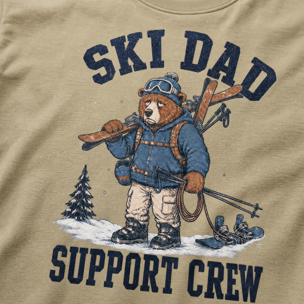 Close-up of a khaki t-shirt with a vintage ski dad design showing an exhausted bear loaded with skis, poles, and snow gear.