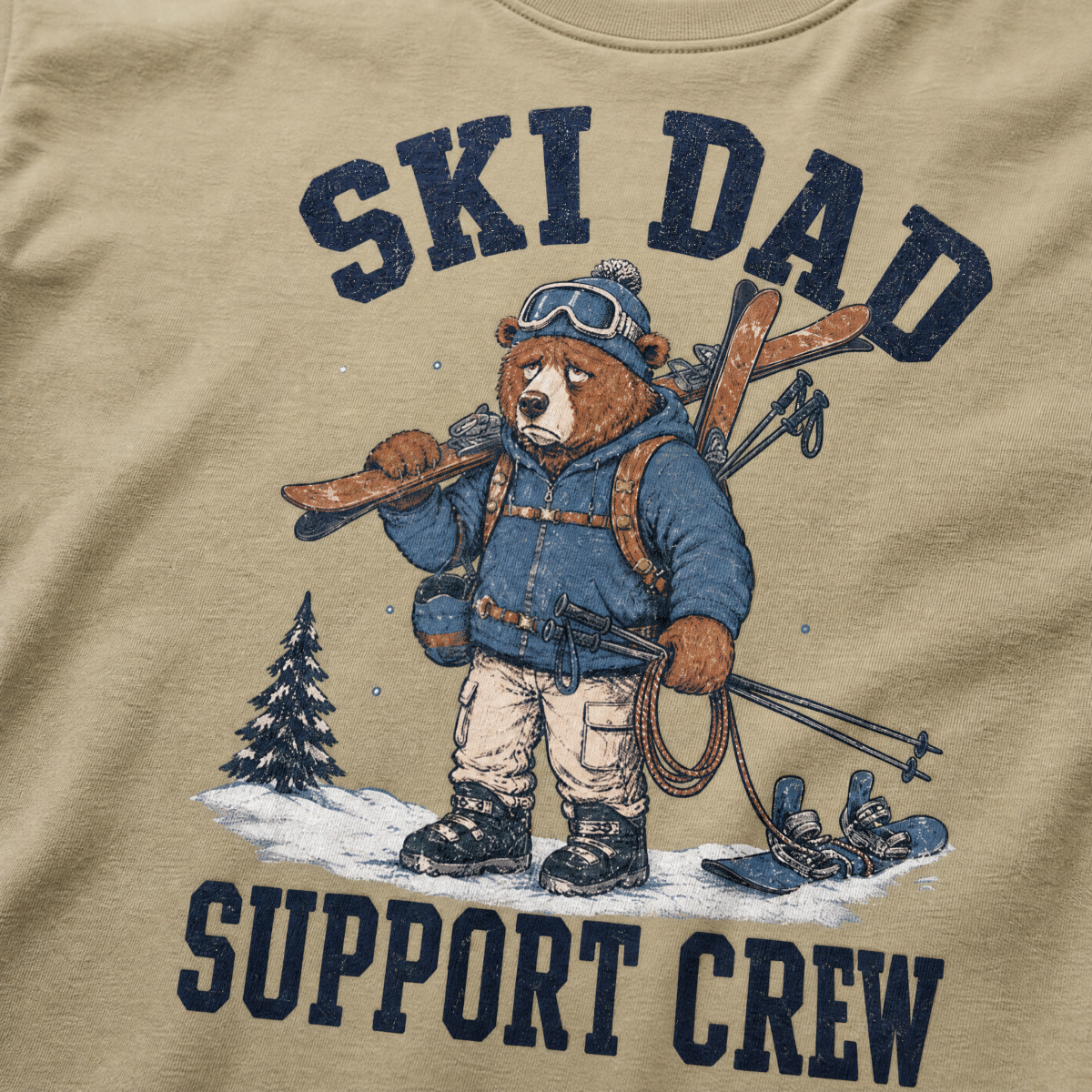 Close-up of a khaki t-shirt with a vintage ski dad design showing an exhausted bear loaded with skis, poles, and snow gear.