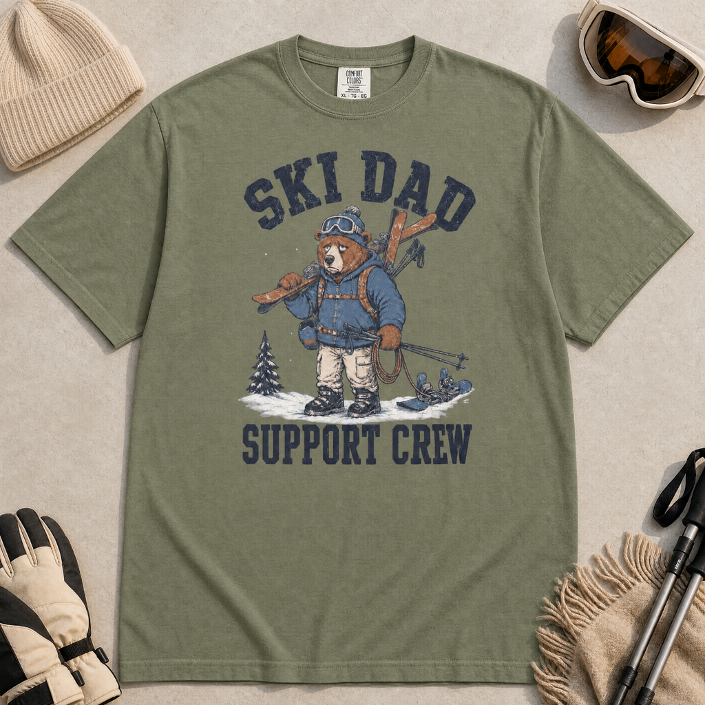 Flat lay of a moss green t-shirt featuring a tired bear carrying skis and ski gear, with “Ski Dad Support Crew” text.