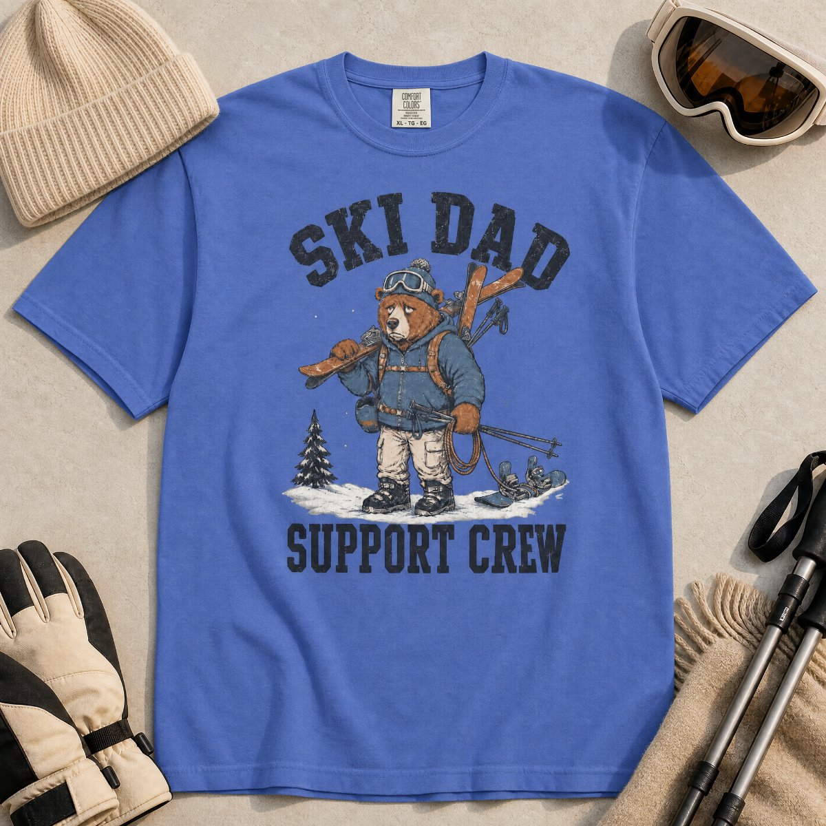 Flat lay of a mystic blue t-shirt featuring a tired bear carrying skis and ski gear, with “Ski Dad Support Crew” text.