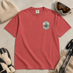 Flat lay of a crimson red t-shirt featuring a small chest “Family Ski Team” badge graphic with three winter animal characters, styled with ski accessories.