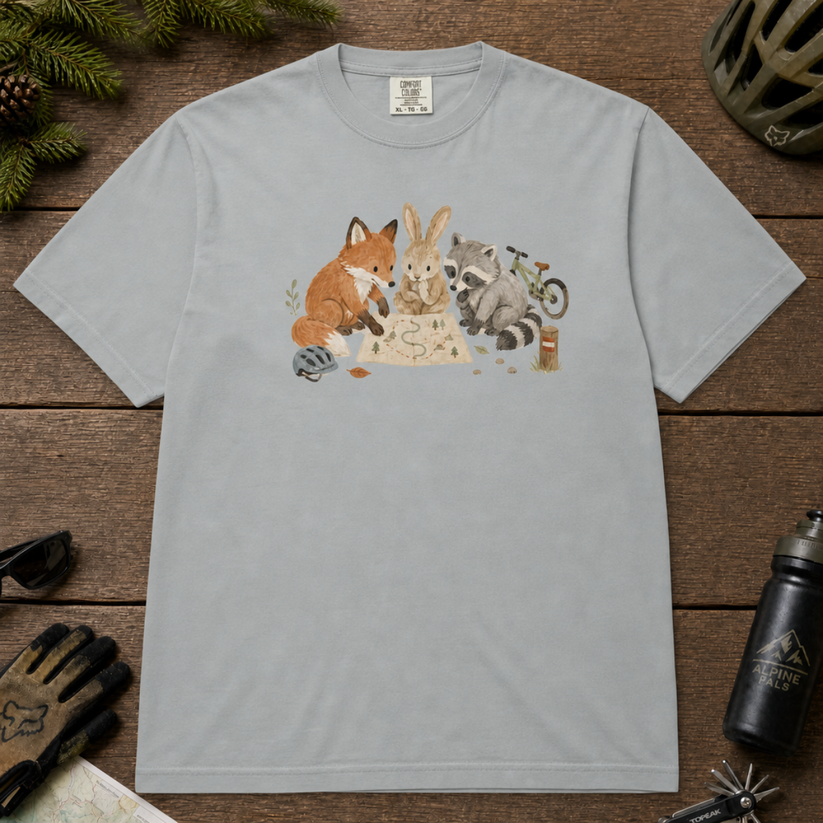 Flat lay of a granite gray t-shirt featuring a cute woodland animal trail-planning graphic with a fox, rabbit, raccoon, map, helmet, bike, and trail marker.