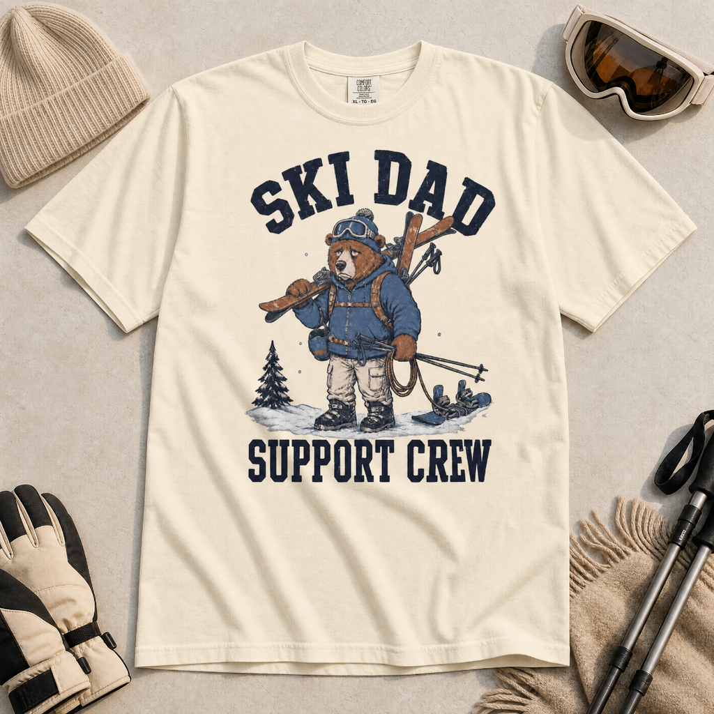 Flat lay of a ivory white t-shirt featuring a tired bear carrying skis and ski gear, with “Ski Dad Support Crew” text.