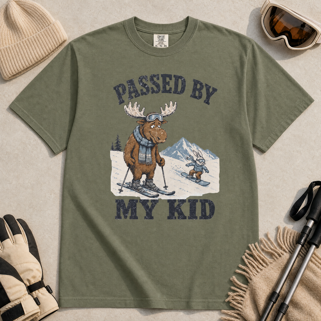 Flat lay of a moss green t-shirt featuring a funny “Passed By My Kid” ski design with a humbled moose watching a small rabbit snowboarder pass by.