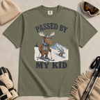 Flat lay of a moss green t-shirt featuring a funny “Passed By My Kid” ski design with a humbled moose watching a small rabbit snowboarder pass by.