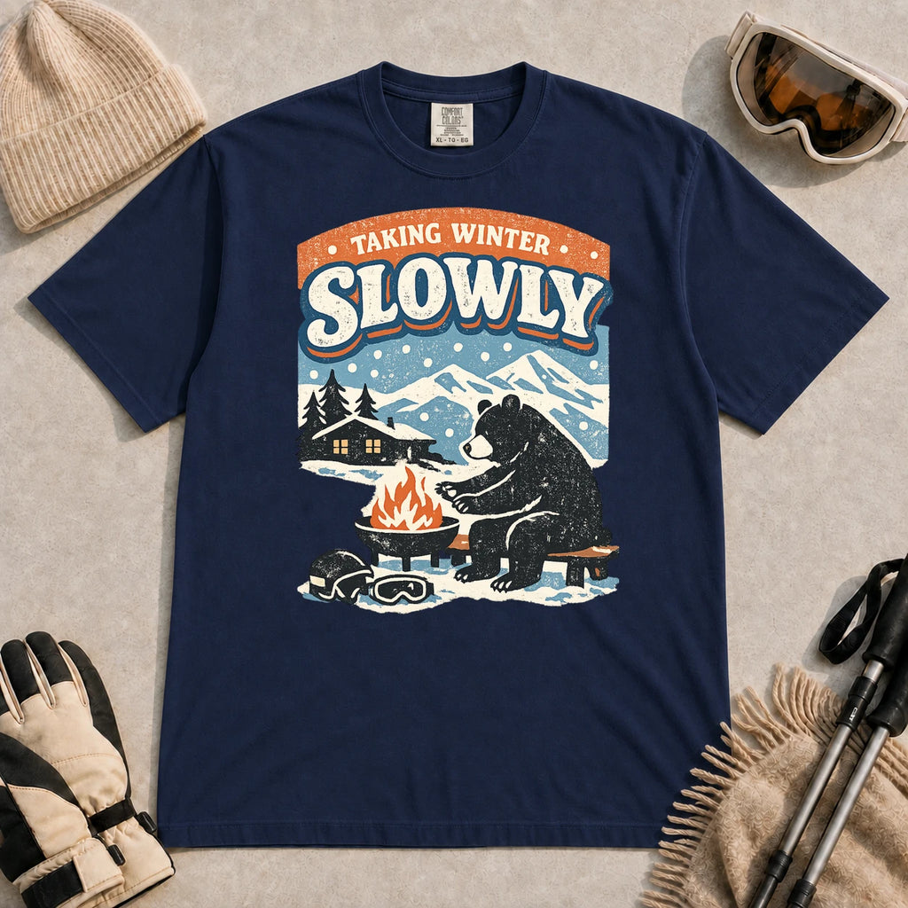 True Navy tee featuring a relaxed bear warming up beside a fire in a snowy mountain setting, with the phrase “Taking Winter Slowly.”
