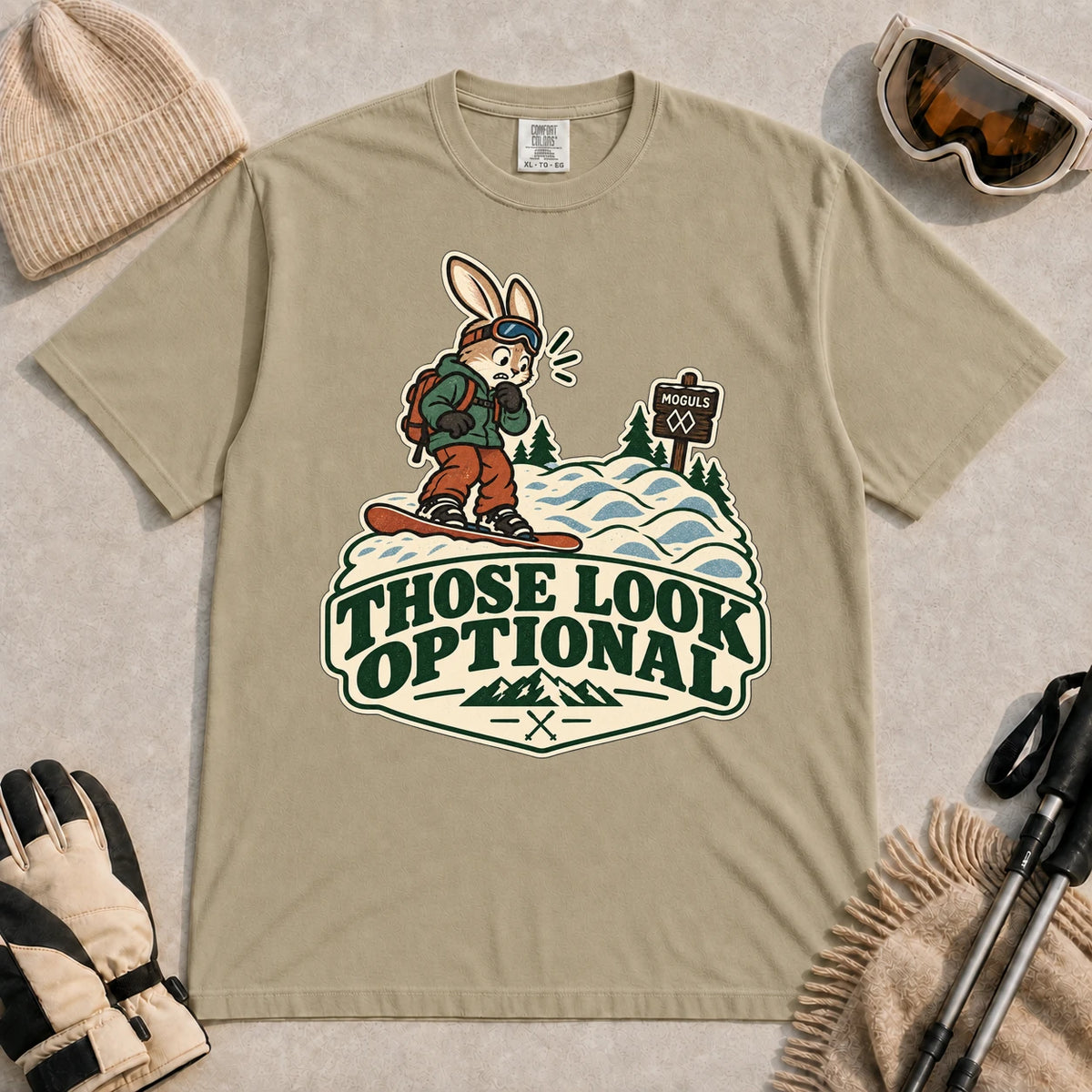 Khaki tee featuring a cautious bunny snowboarder facing a mogul run beside a “Moguls” sign above the phrase “Those Look Optional.”