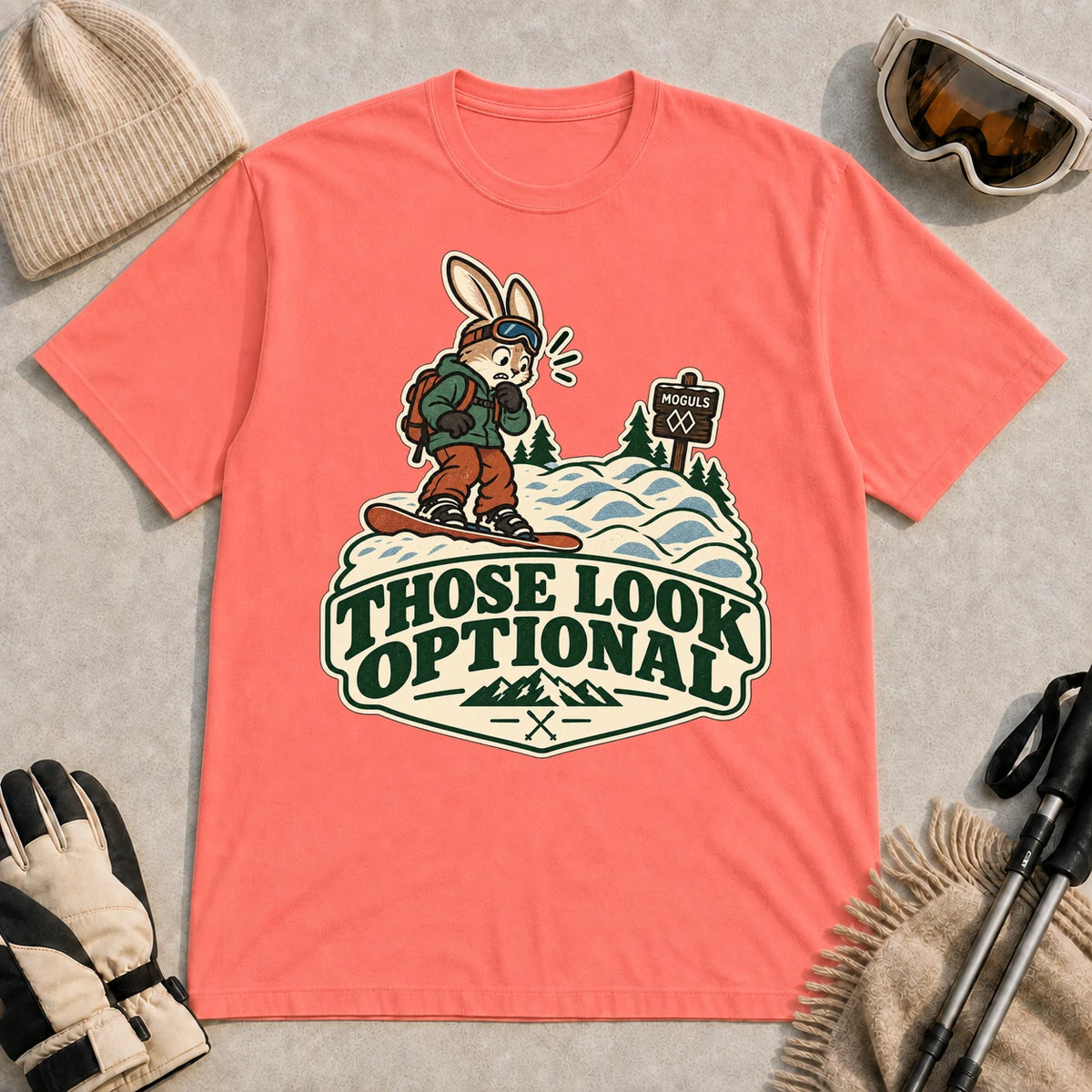 Coral Silk tee featuring a cautious bunny snowboarder facing a mogul run beside a “Moguls” sign above the phrase “Those Look Optional.”