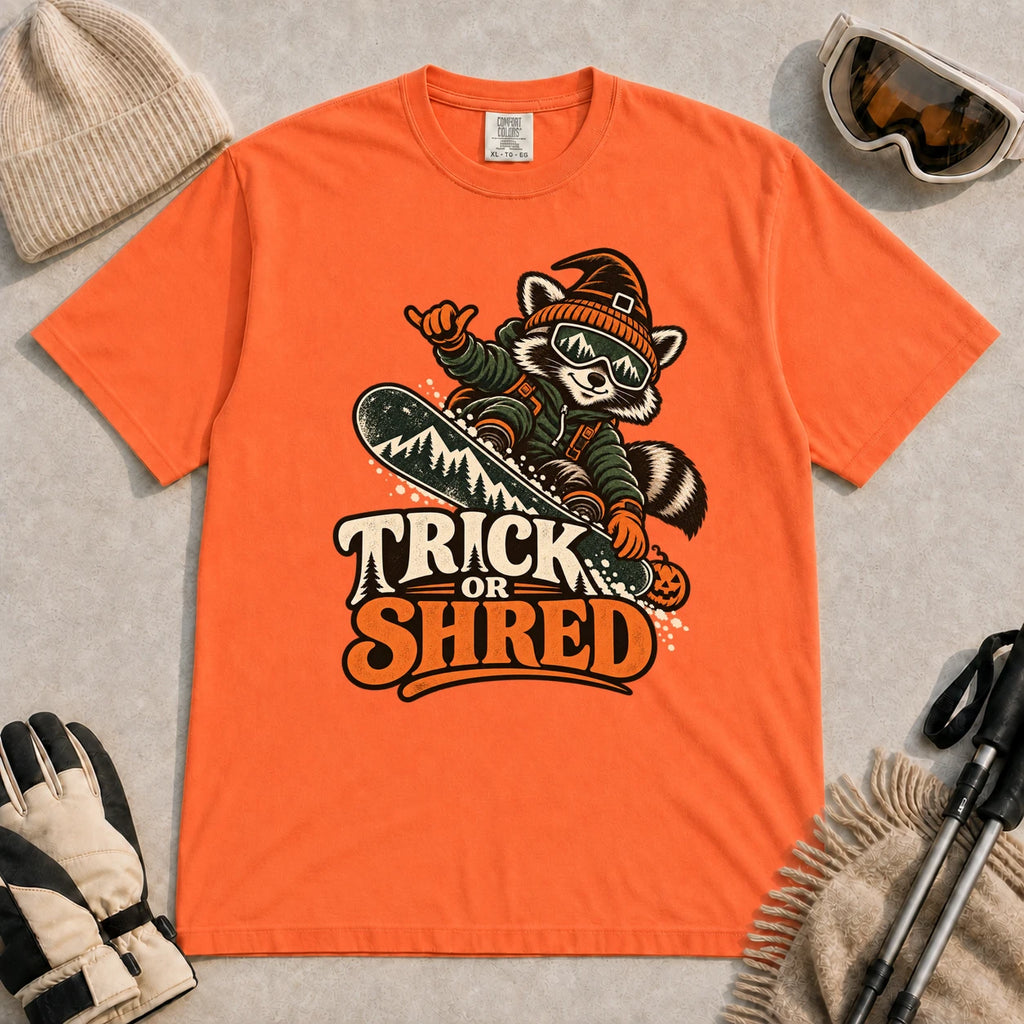 Burnt Orange tee featuring a raccoon snowboarding in Halloween gear and a witch hat above the phrase “Trick or Shred.”