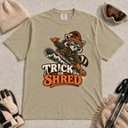 Khaki tee featuring a raccoon snowboarding in Halloween gear and a witch hat above the phrase “Trick or Shred.”
