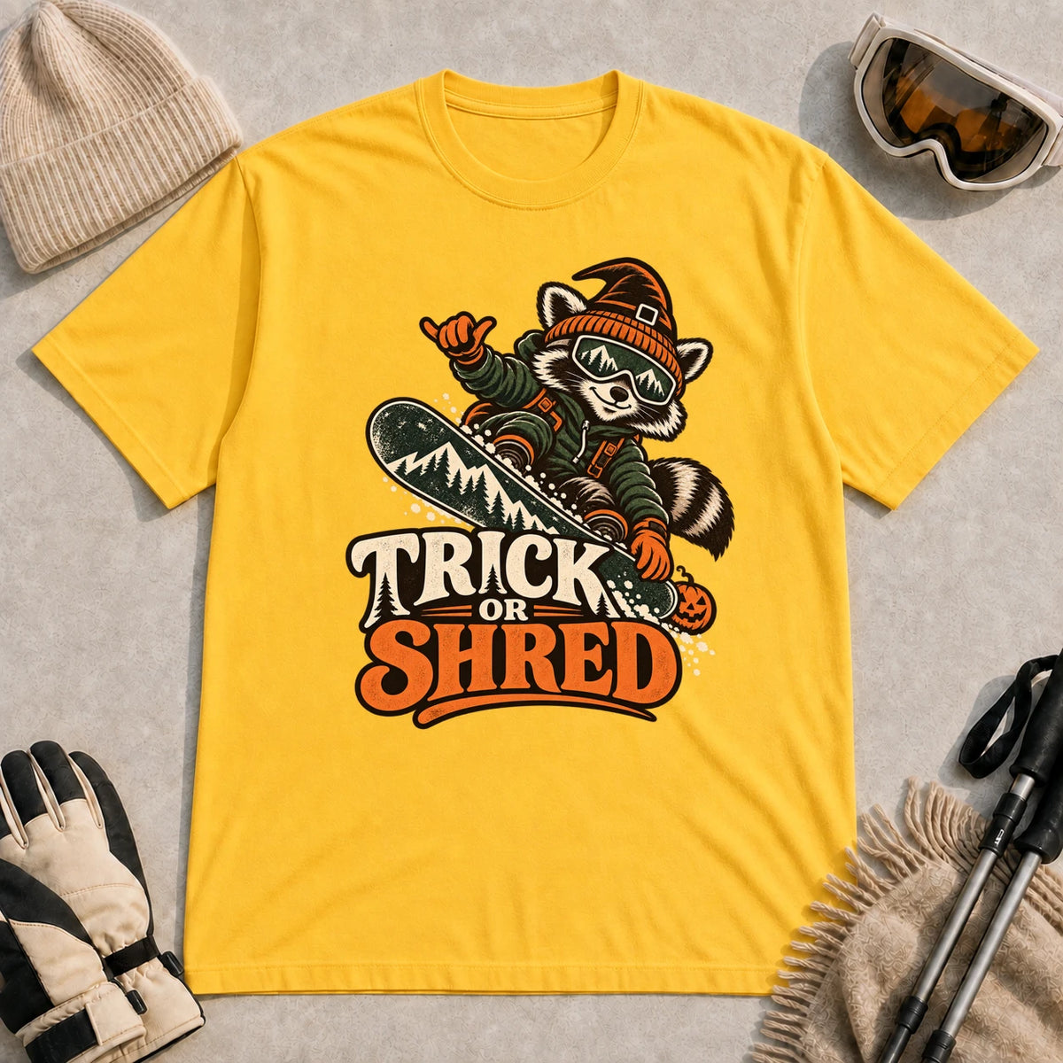 Daisy tee featuring a raccoon snowboarding in Halloween gear and a witch hat above the phrase “Trick or Shred.”