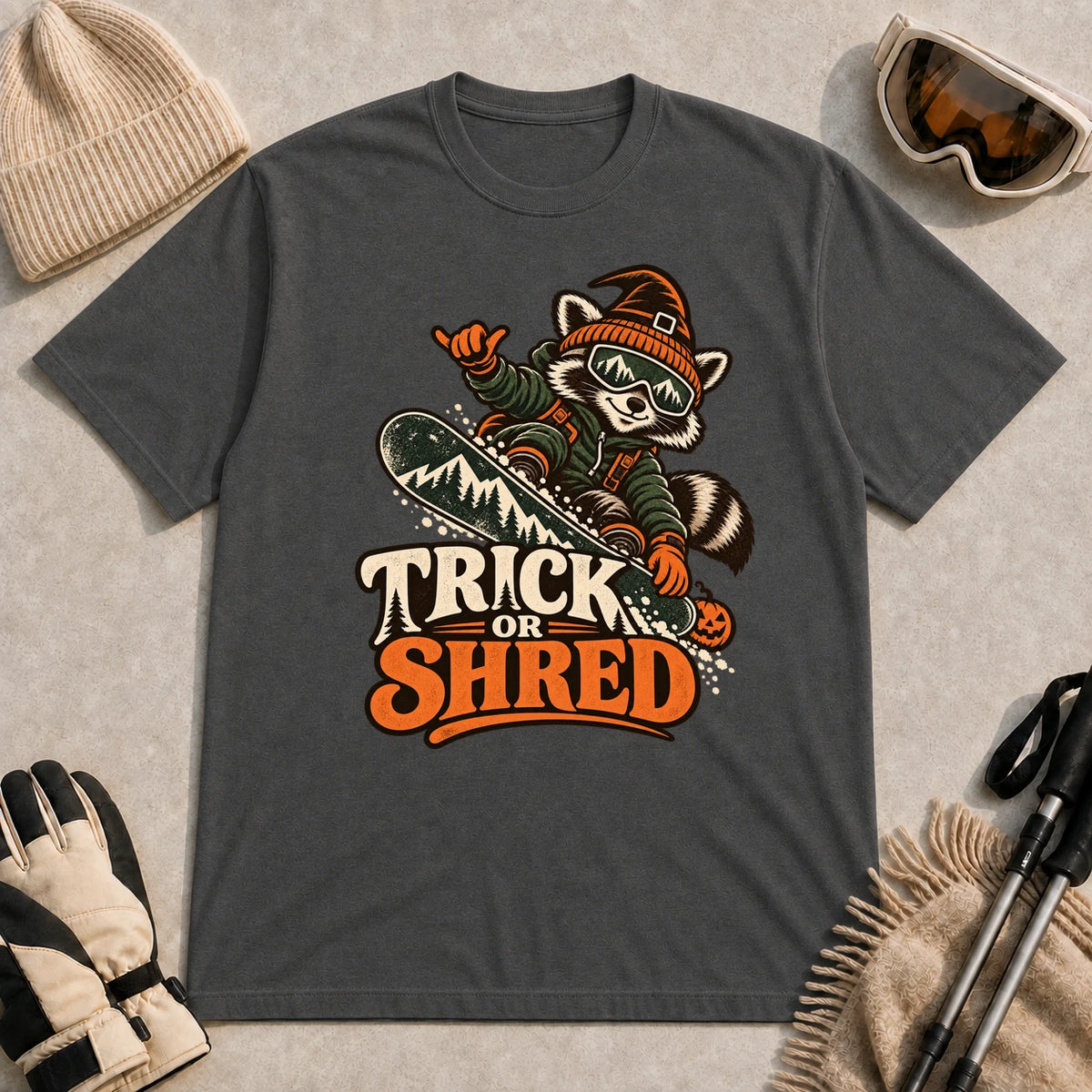 Dark Heather Gray tee featuring a raccoon snowboarding in Halloween gear and a witch hat above the phrase “Trick or Shred.”