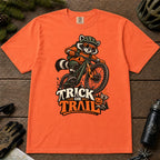 Burnt Orange tee featuring a raccoon mountain biking in Halloween gear above a pumpkin and trail sign, with the phrase “Trick or Trail.”