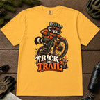 Mustard tee featuring a raccoon mountain biking in Halloween gear above a pumpkin and trail sign, with the phrase “Trick or Trail.”