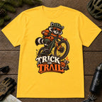 Daisy tee featuring a raccoon mountain biking in Halloween gear above a pumpkin and trail sign, with the phrase “Trick or Trail.”
