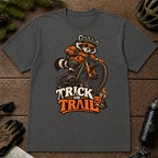 Dark Heather Gray tee featuring a raccoon mountain biking in Halloween gear above a pumpkin and trail sign, with the phrase “Trick or Trail.”
