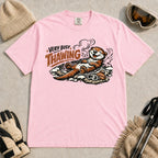 Blossom tee featuring a relaxed otter thawing in a warm mountain hot spring beside ski goggles and a beanie, with the phrase “Very Busy Thawing.”
