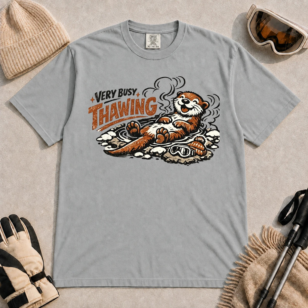 Granite tee featuring a relaxed otter thawing in a warm mountain hot spring beside ski goggles and a beanie, with the phrase “Very Busy Thawing.”