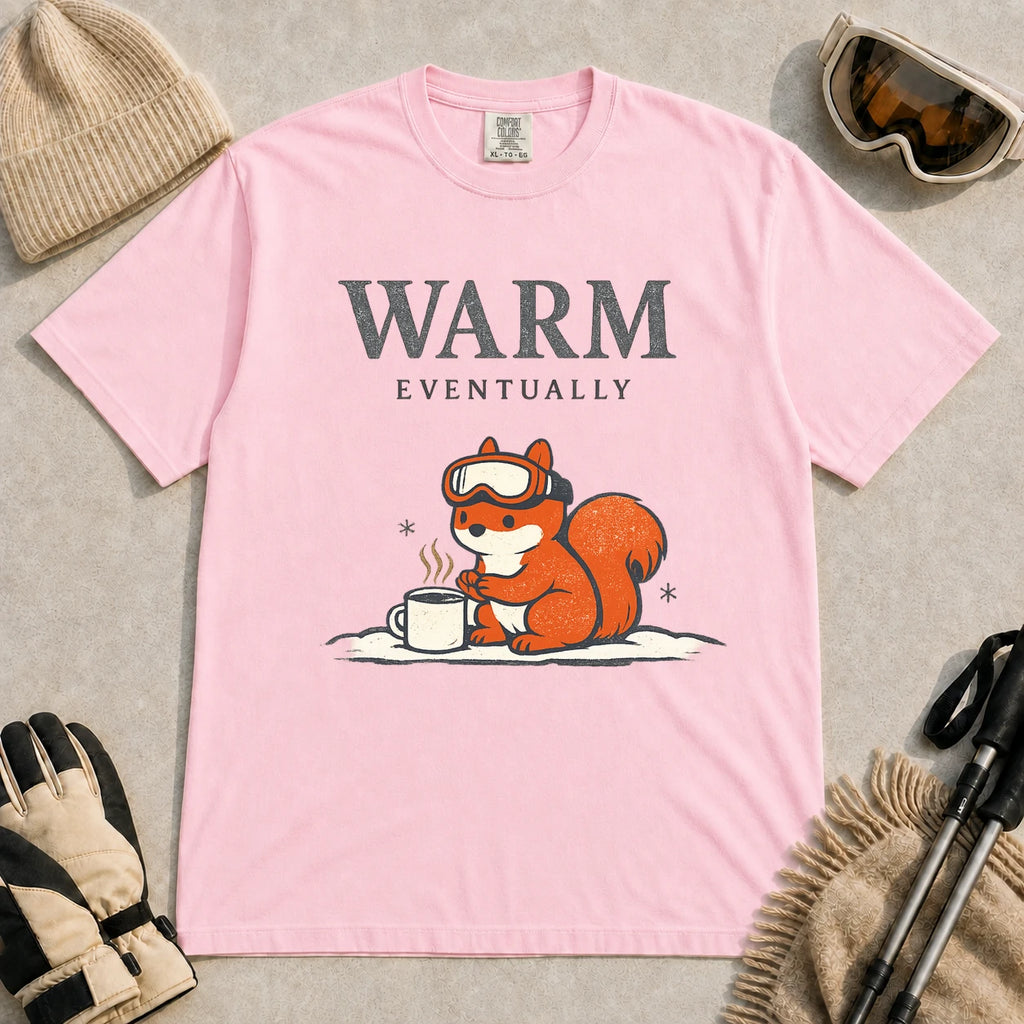 Blossom tee featuring a chilly squirrel in ski goggles warming its paws beside a steaming mug in the snow, with the phrase “Warm Eventually.”