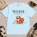 Chambray tee featuring a chilly squirrel in ski goggles warming its paws beside a steaming mug in the snow, with the phrase “Warm Eventually.”