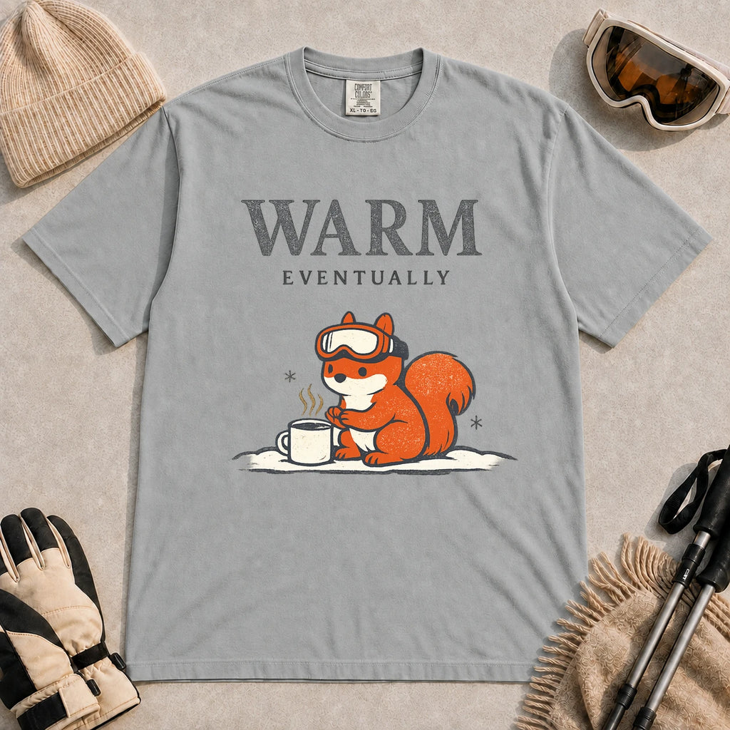 Granite tee featuring a chilly squirrel in ski goggles warming its paws beside a steaming mug in the snow, with the phrase “Warm Eventually.”