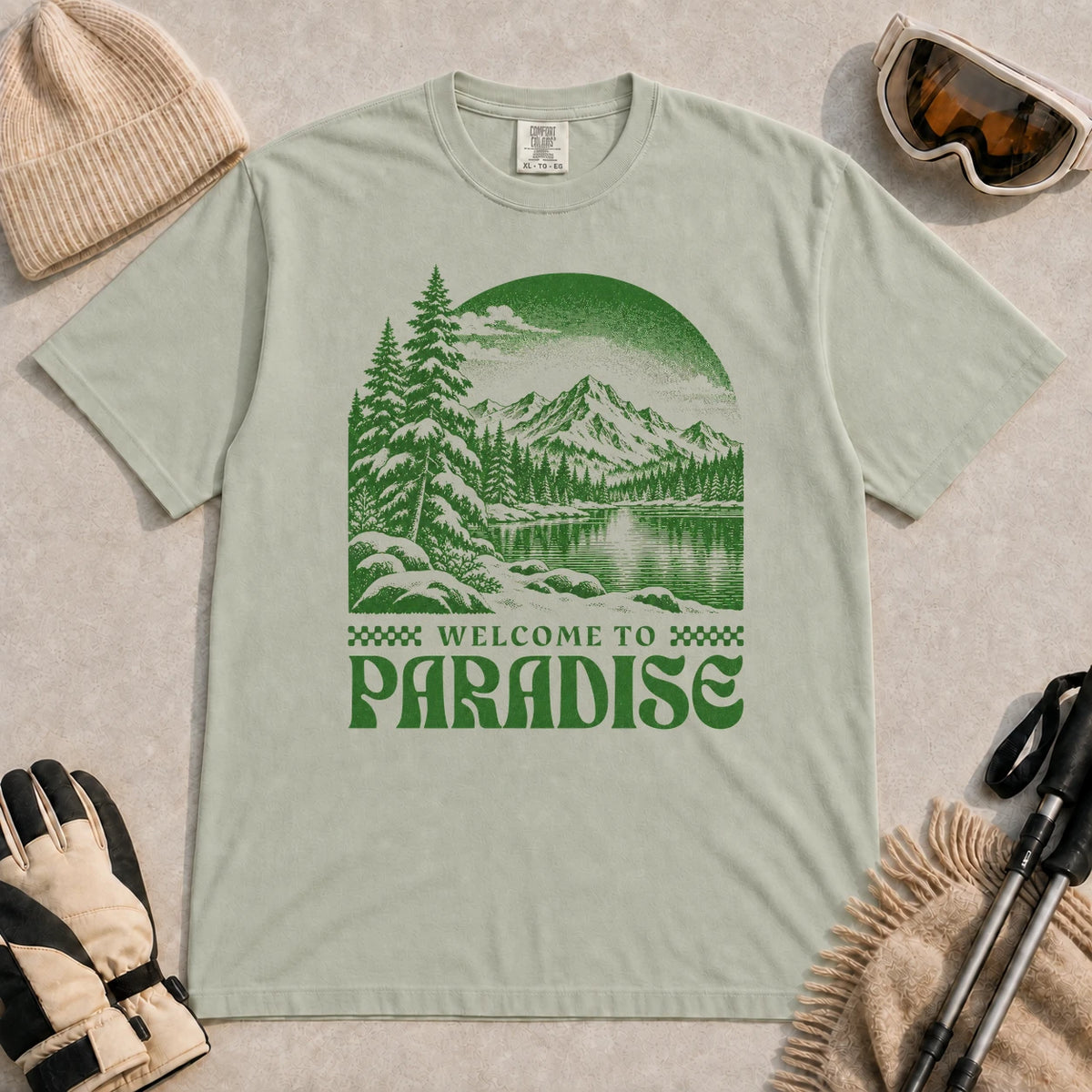 Bay tee featuring a green vintage mountain lake and evergreen forest scene with the phrase “Welcome to Paradise.”