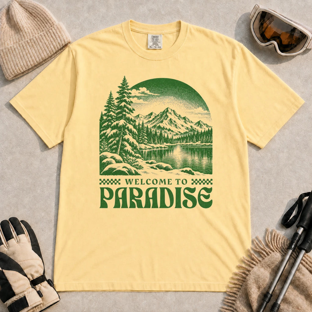 Butter tee featuring a green vintage mountain lake and evergreen forest scene with the phrase “Welcome to Paradise.”