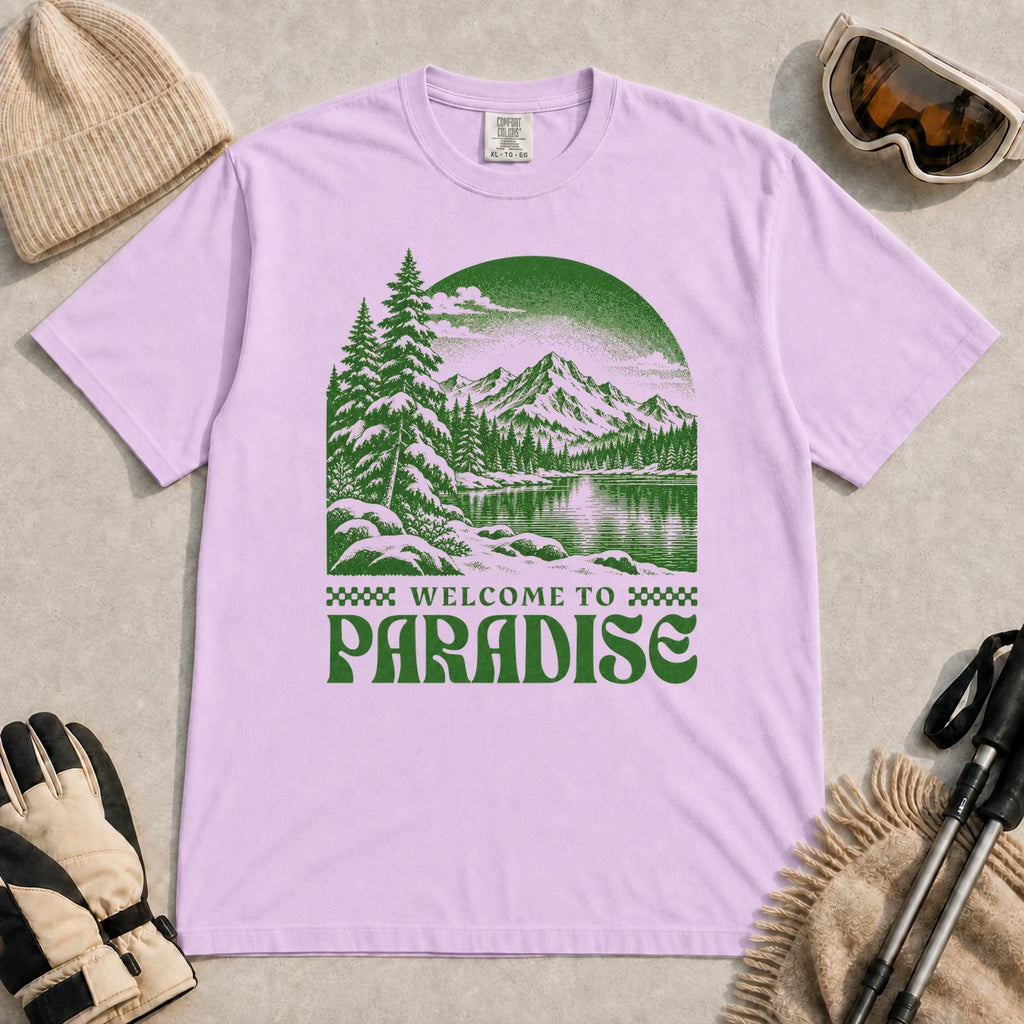 Orchid tee featuring a green vintage mountain lake and evergreen forest scene with the phrase “Welcome to Paradise.”