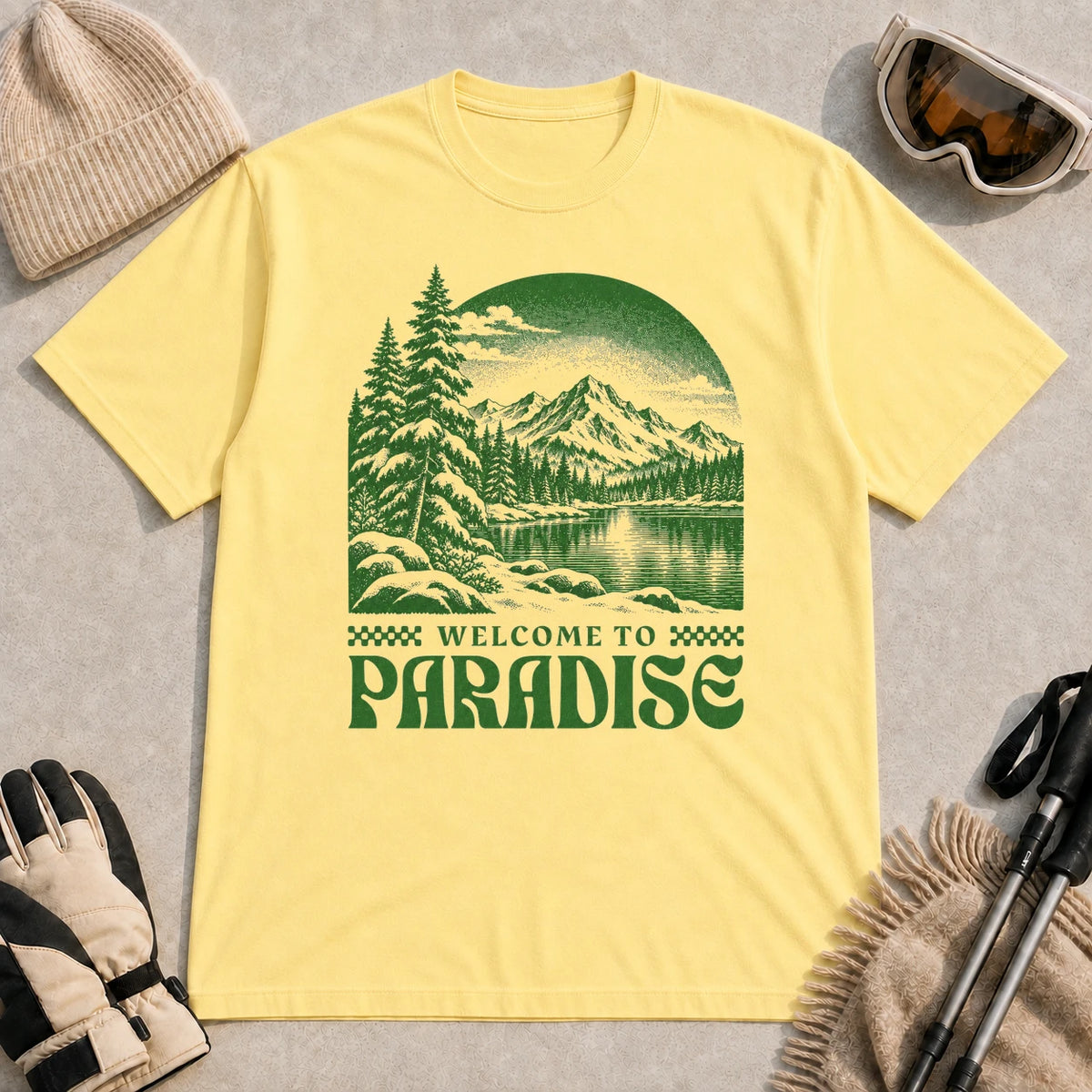 Cornsilk tee featuring a green vintage mountain lake and evergreen forest scene with the phrase “Welcome to Paradise.”