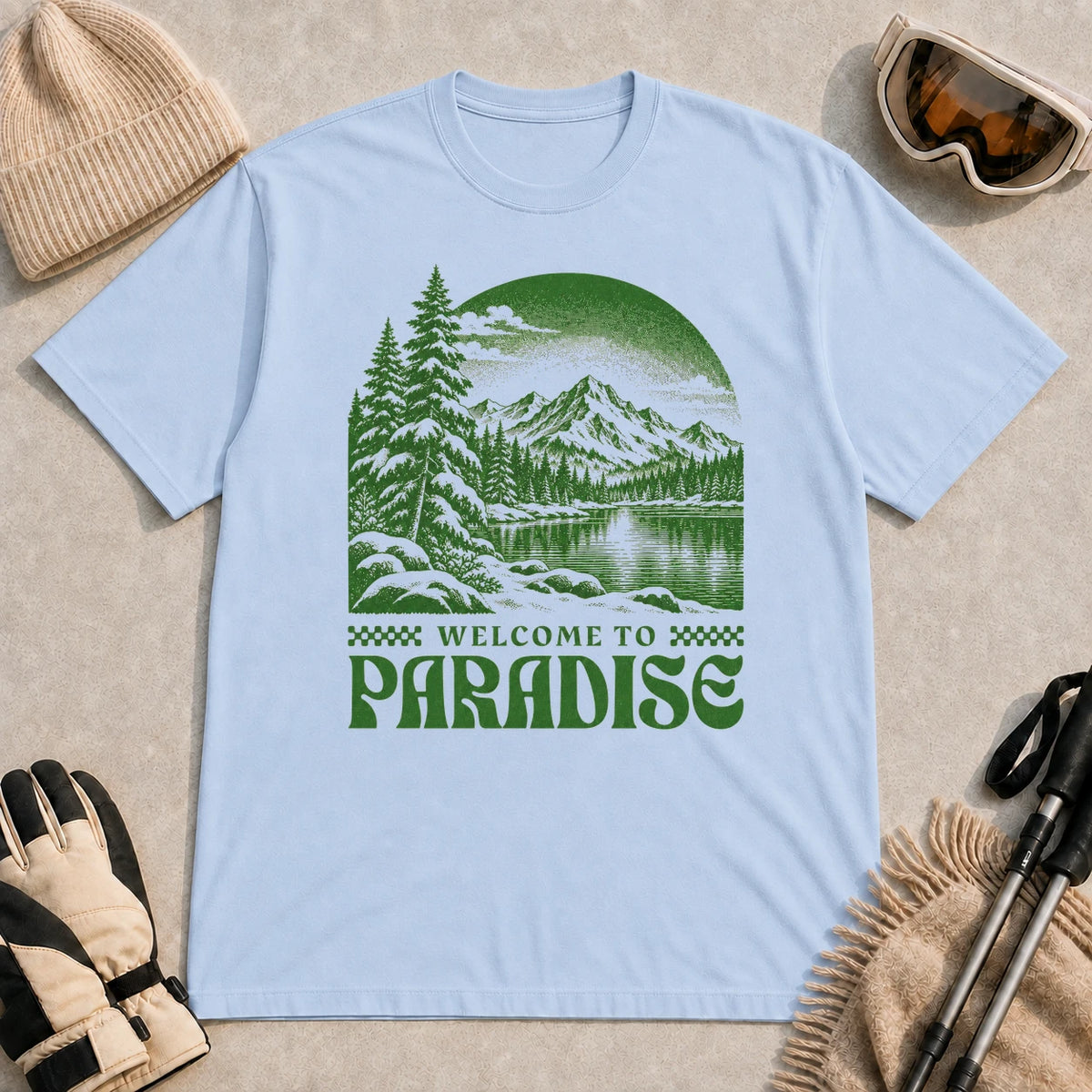 Light Blue tee featuring a green vintage mountain lake and evergreen forest scene with the phrase “Welcome to Paradise.”