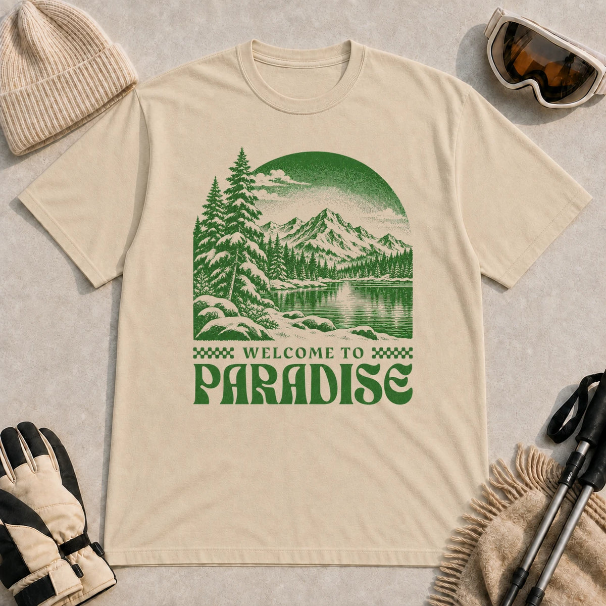 Sand tee featuring a green vintage mountain lake and evergreen forest scene with the phrase “Welcome to Paradise.”