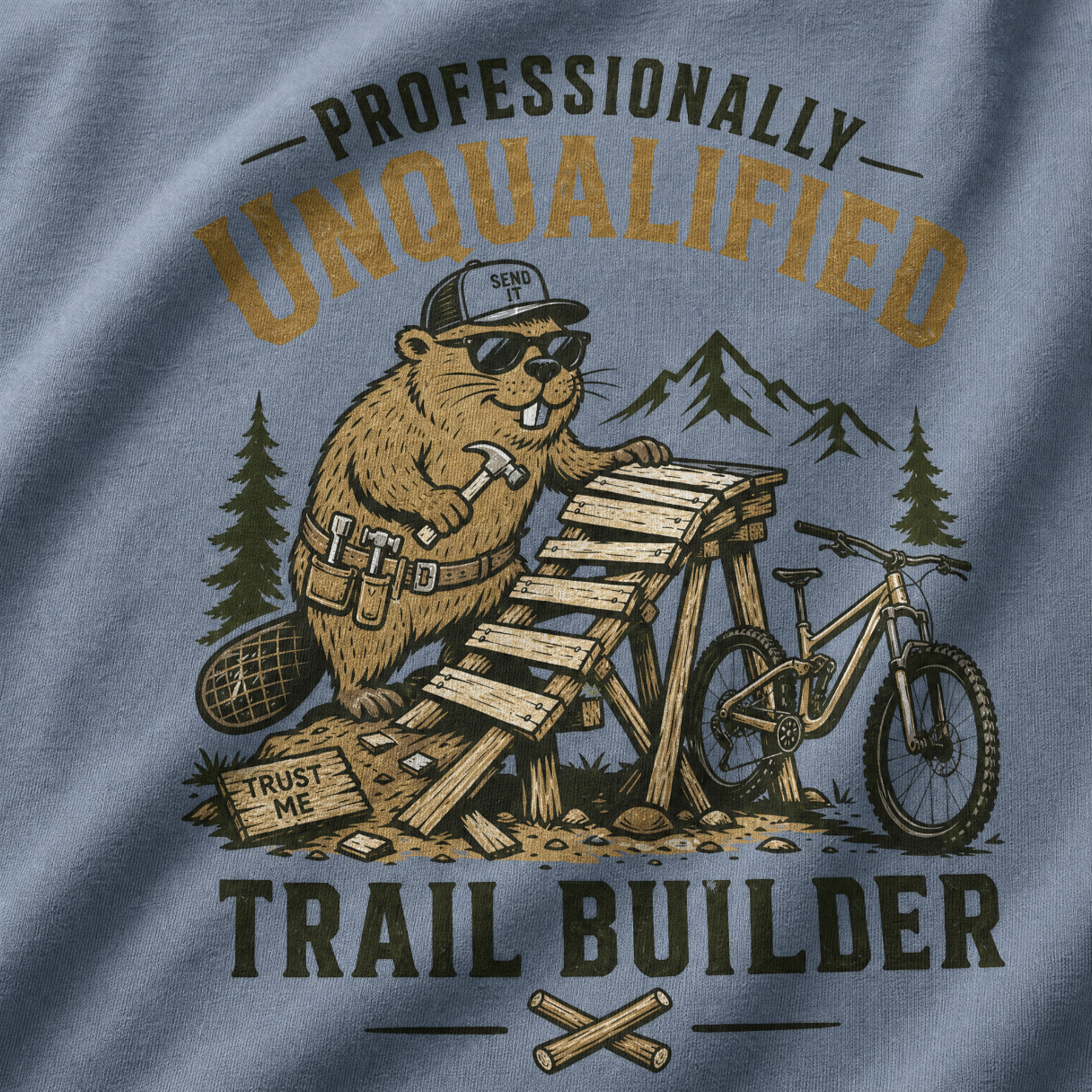 T-shirt design with beaver character and mountain bike, text 'Professionally Unqualified Trail Builder' on blue fabric.