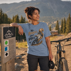 Woman in a blue t-shirt with a bicycle graphic and text, standing next to a bike in a mountainous area.