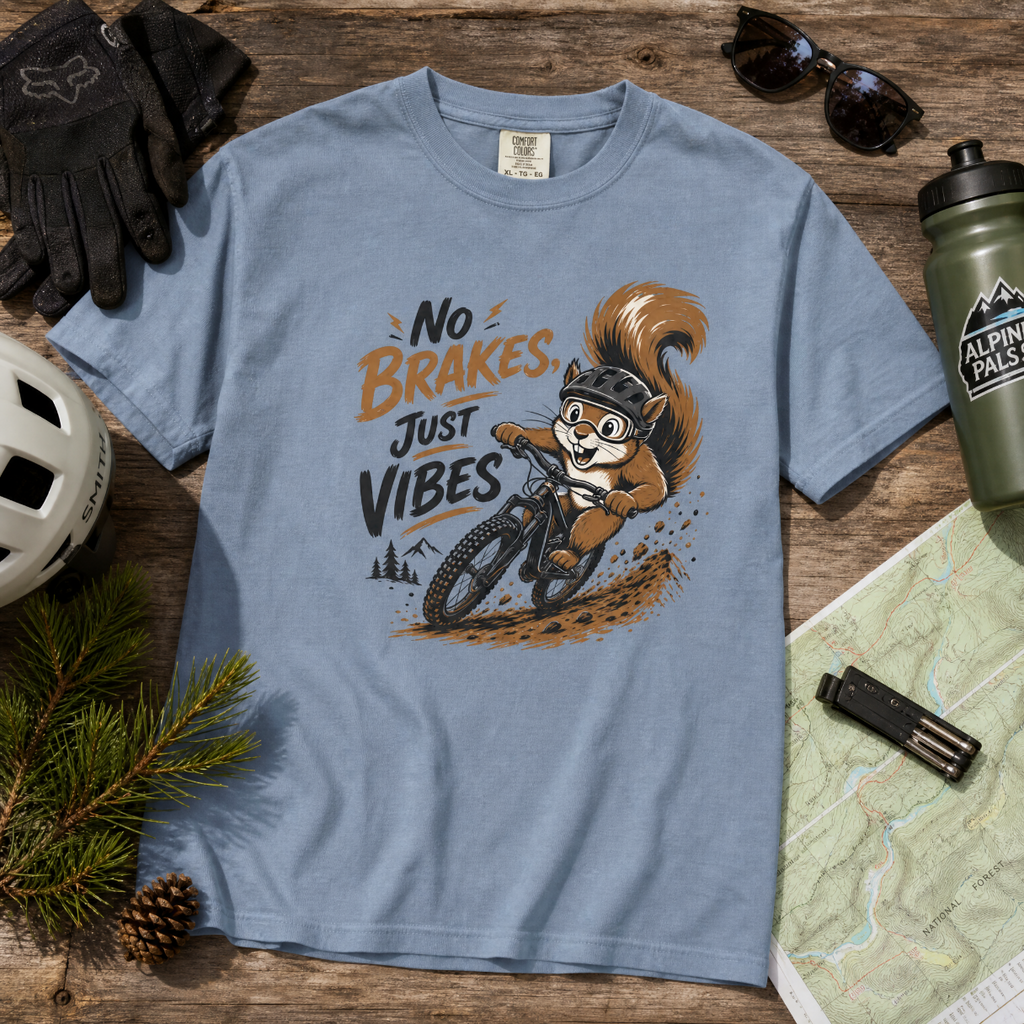 Blue t-shirt with a squirrel graphic and 'No Brakes, Just Vibes' text on a wooden surface with outdoor gear.