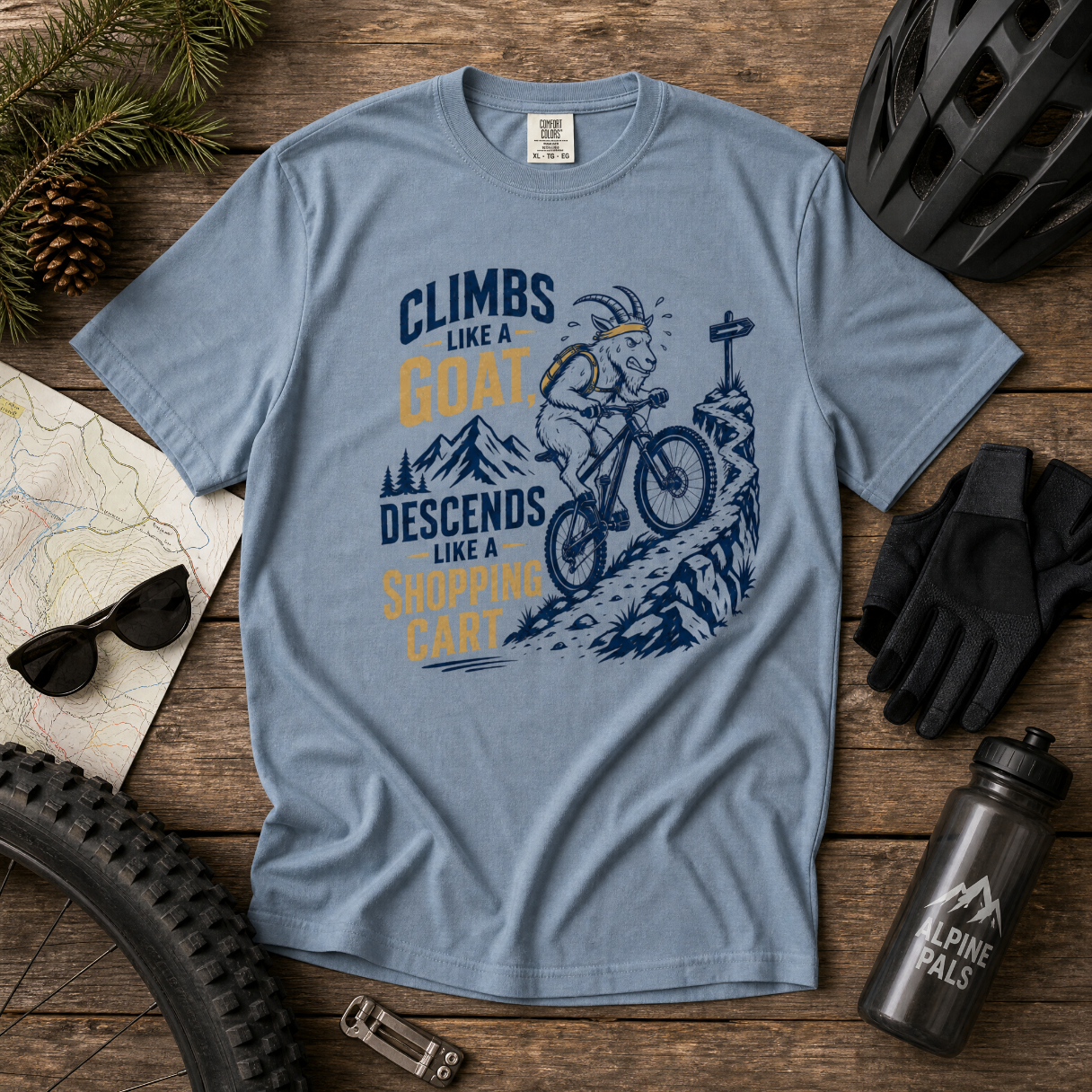 Blue jean colored t-shirt with graphic design and text on a wooden surface with cycling accessories.