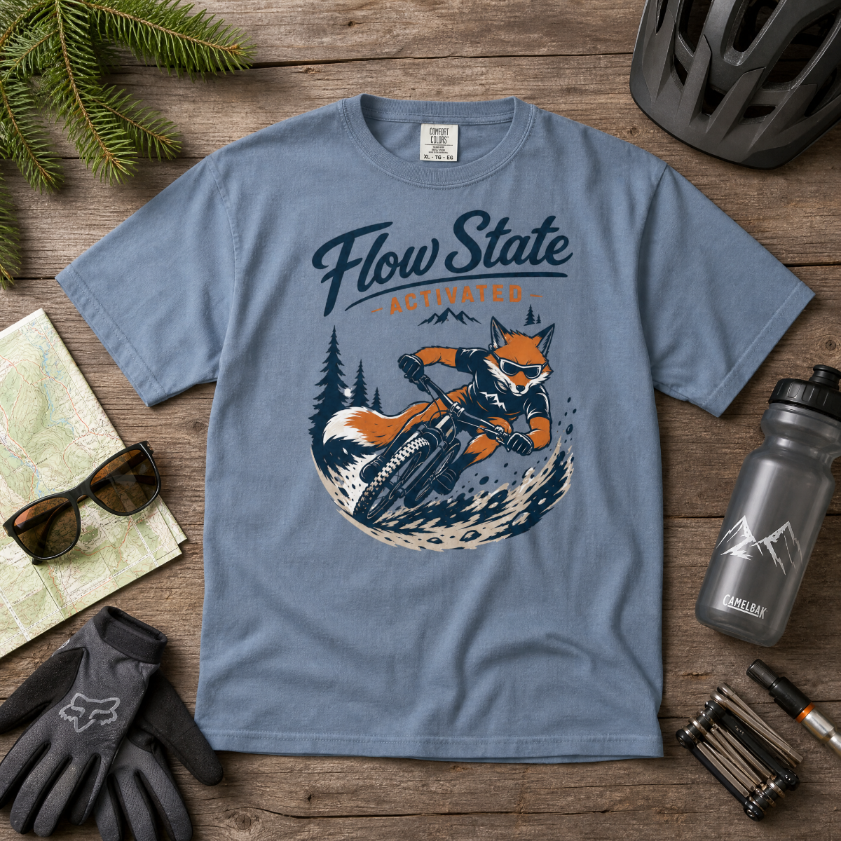 Blue t-shirt with fox graphic and 'Flow State Activated' text on a wooden surface with accessories.