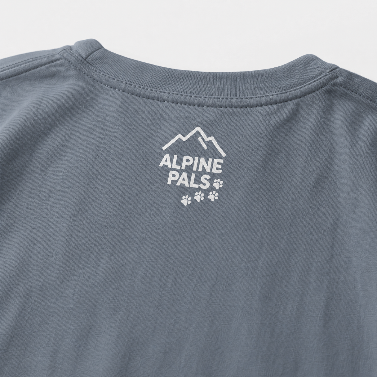Blue jean colored shirt with 'Alpine Pals' logo on a light gray background