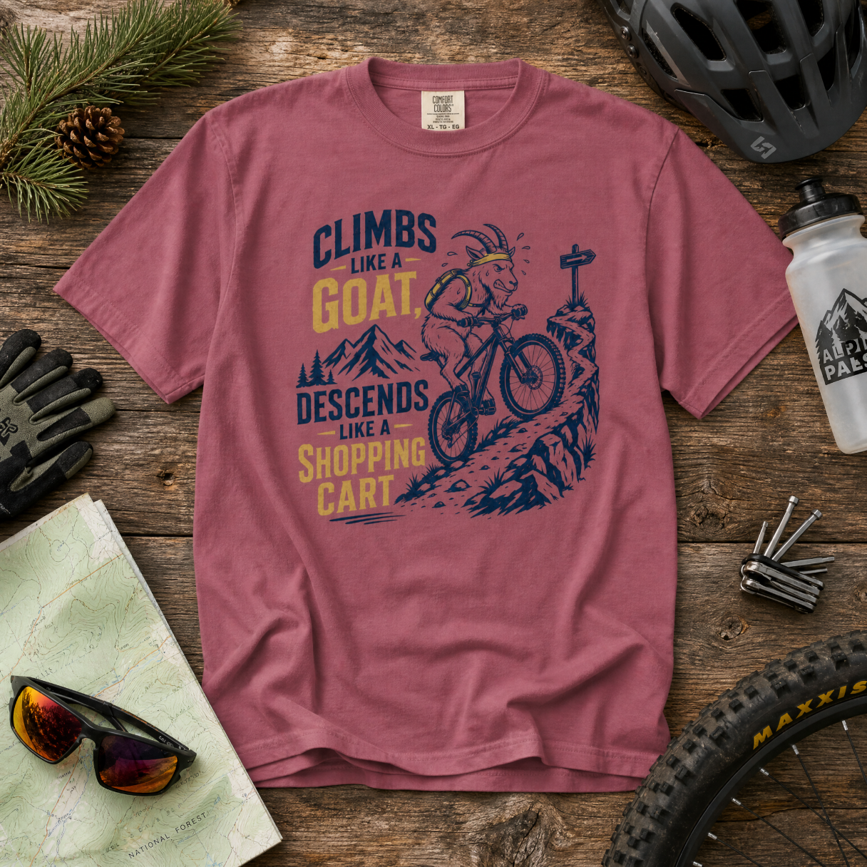 Brick colored t-shirt with mountain bike graphic and text on a wooden surface with cycling accessories.