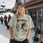 Person wearing a 'Hot Doggin' t-shirt with a snowboarding graphic in a snowy resort setting.