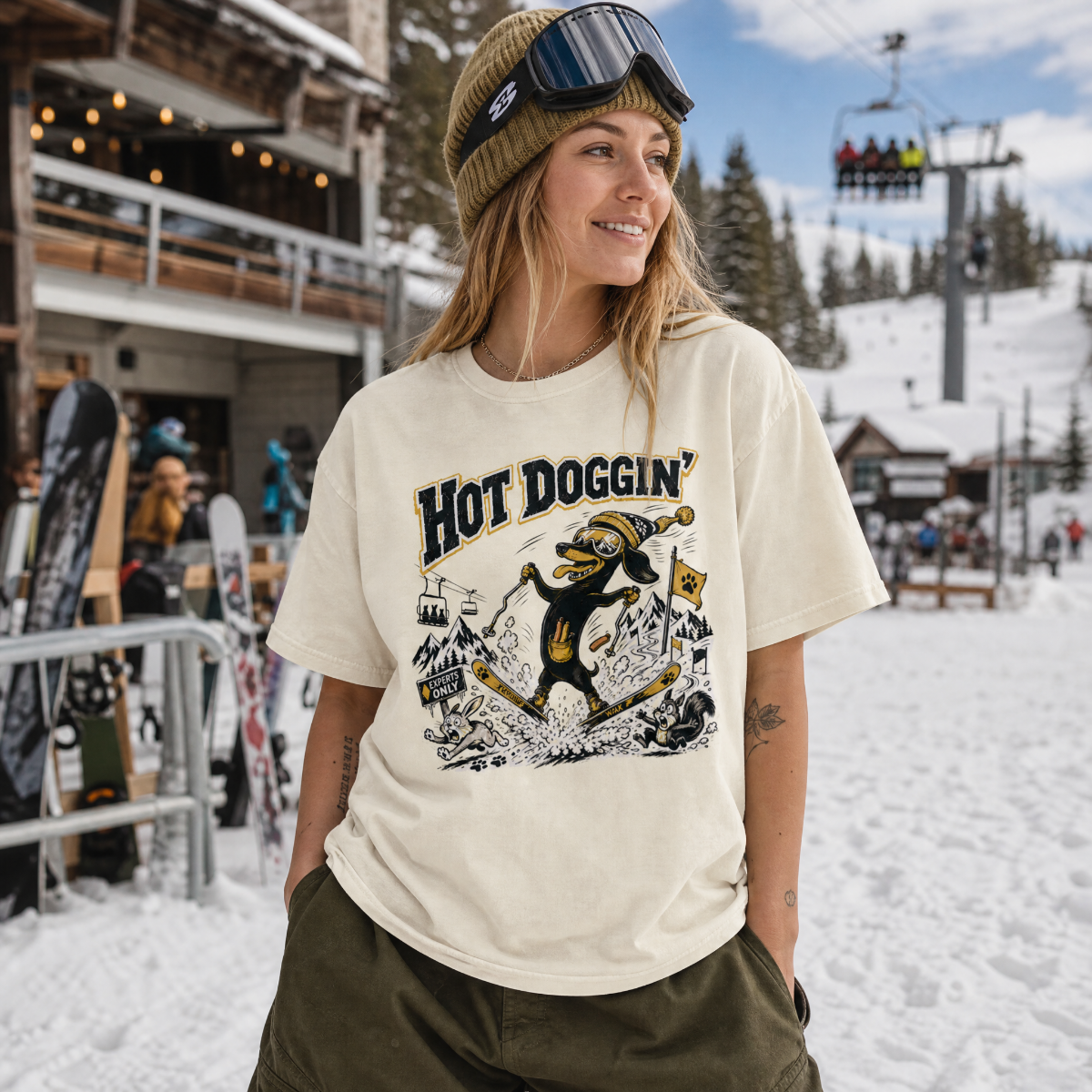 Person wearing a 'Hot Doggin' t-shirt at a snowy ski resort.